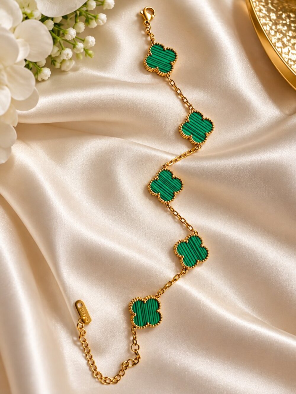 Gold-tone bracelet featuring five four-leaf clover charms with rich emerald-gree